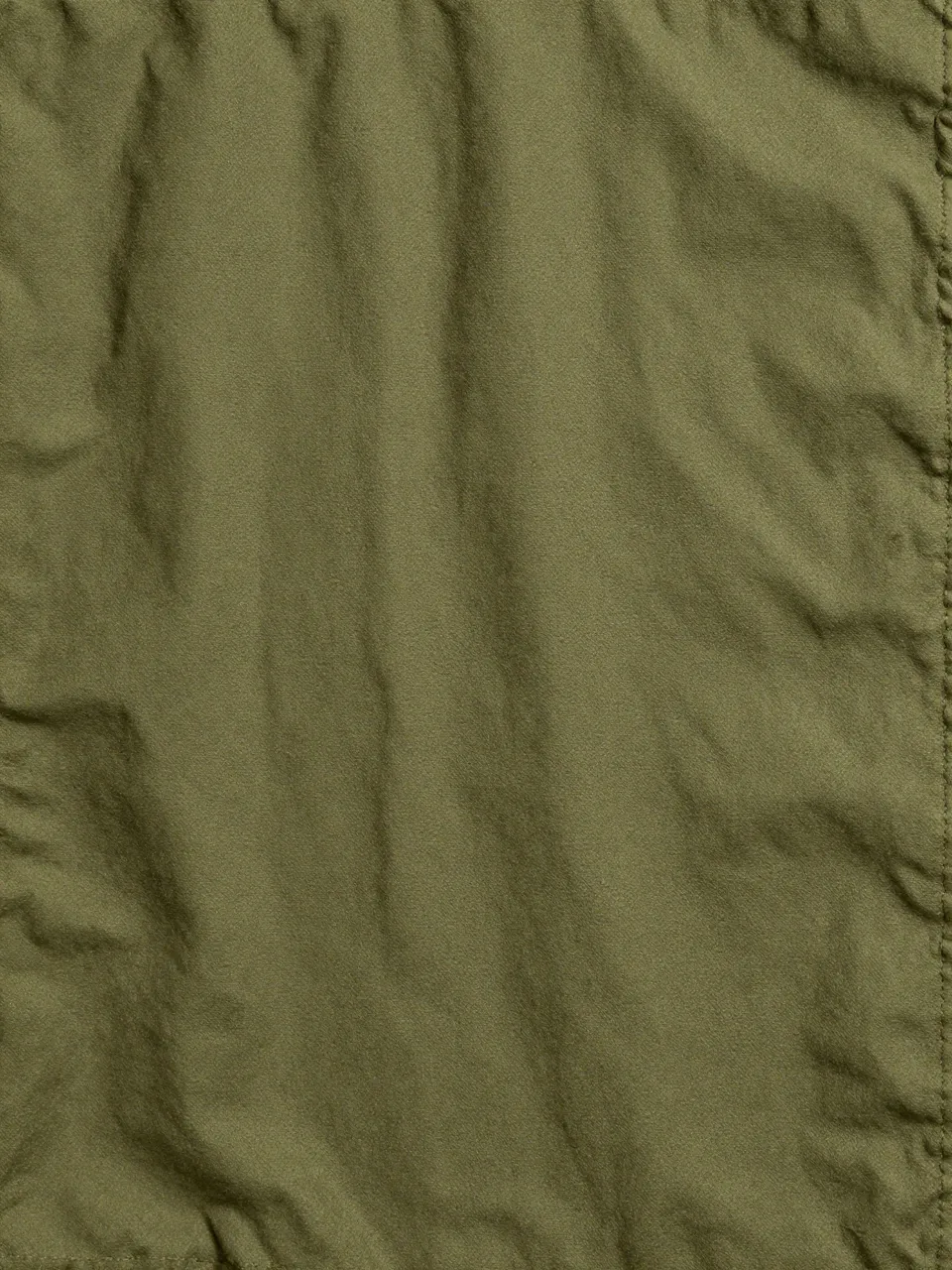 Full frame close-up of wrinkled olive green waxed canvas with soft natural creases