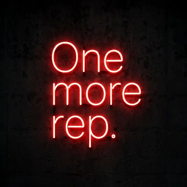 Glowing red neon sign reading "One more rep." mounted on a dark textured concrete wall