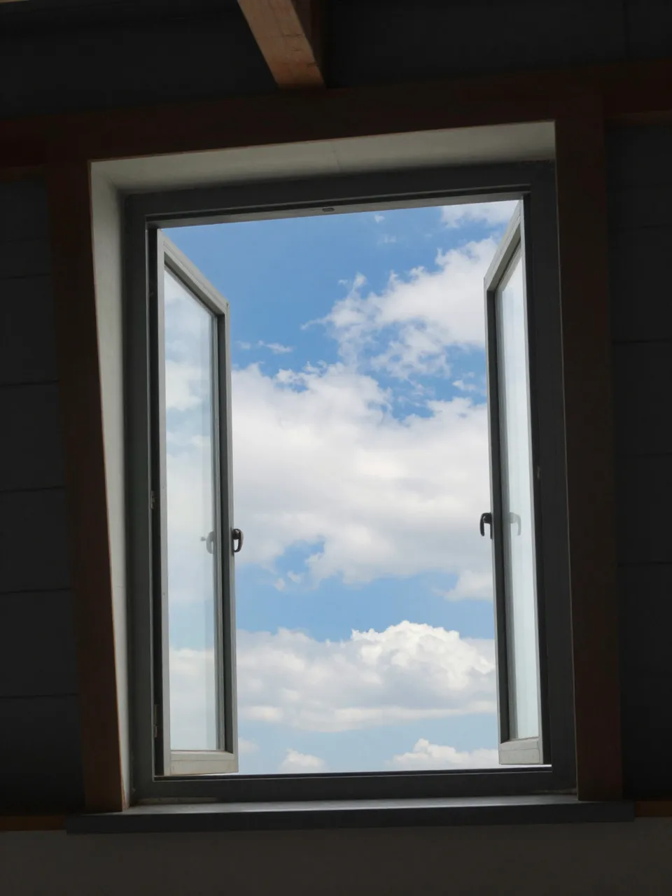 Open attic window frames a bright blue sky with soft drifting white clouds