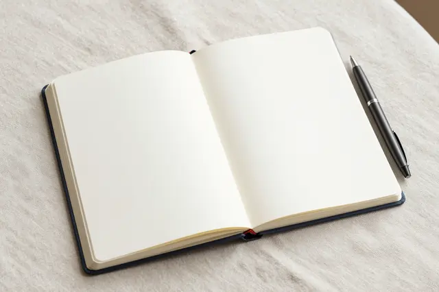 An open blank notebook with a pen rests on a soft linen tablecloth in gentle natural light