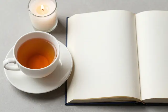 An open blank lined notebook sits next to a teacup and a lit tealight candle on a gray tabletop.