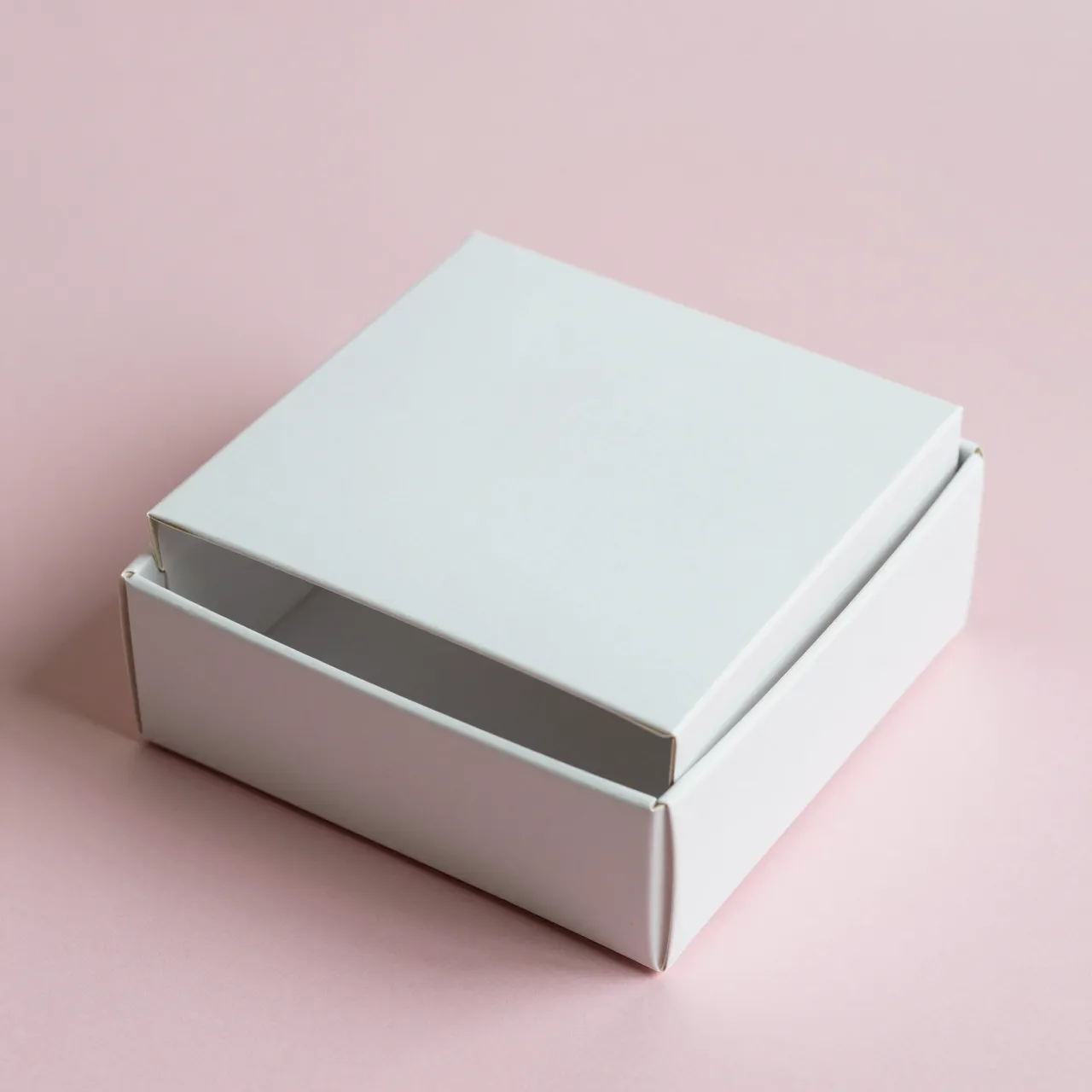 Plain white square product box with a slightly ajar lid rests on a smooth pastel pink background