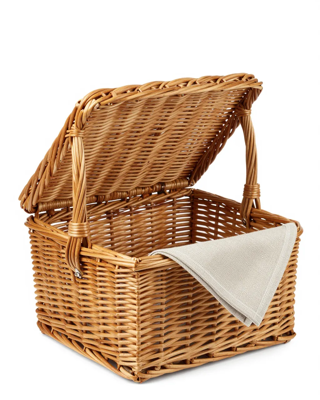 Light brown wicker picnic basket with open lid and folded linen napkin on a plain white studio background