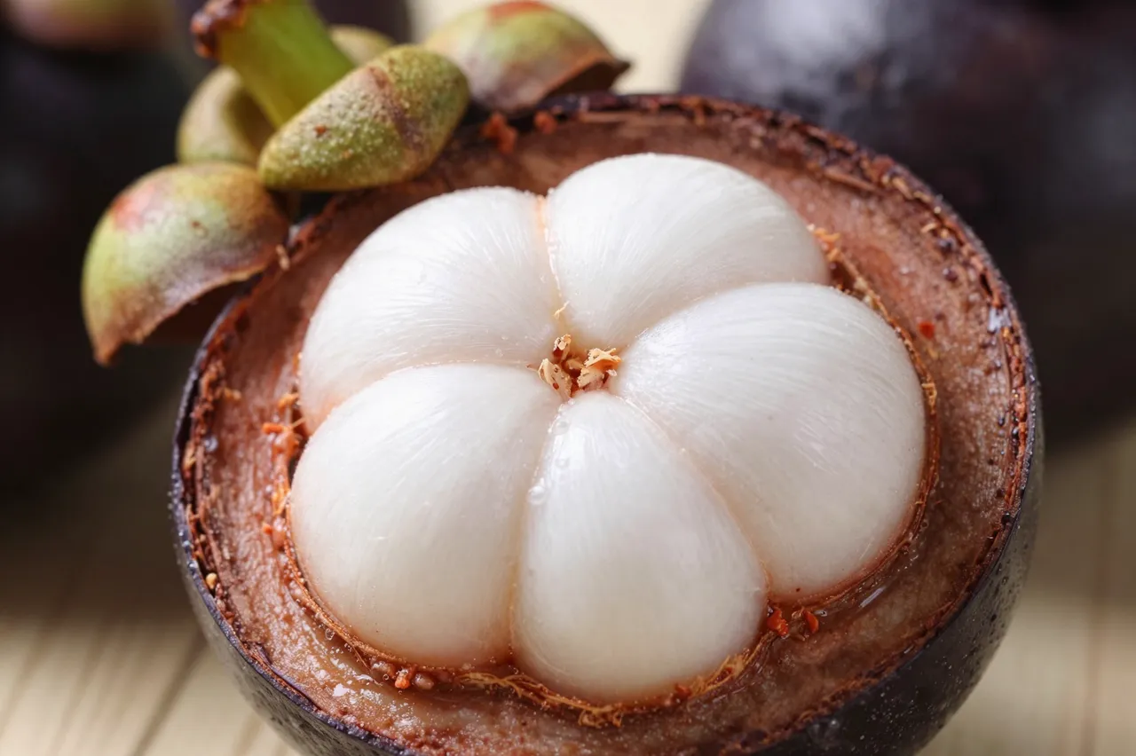 Close-up of a halved mangosteen showing smooth white fleshy segments inside its dark rind