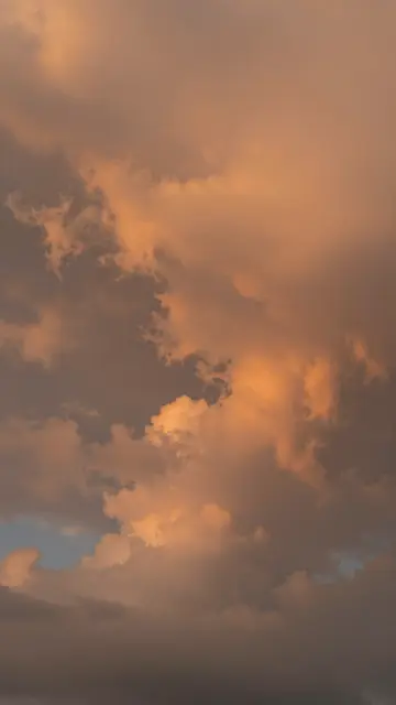 Towering storm clouds glow warm orange as they catch the light of a setting sun