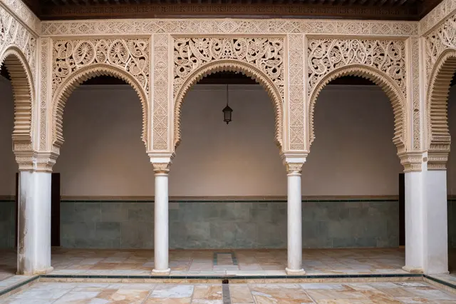 Intricately carved plaster horseshoe arches line a quiet Andalusian courtyard with tiled floors