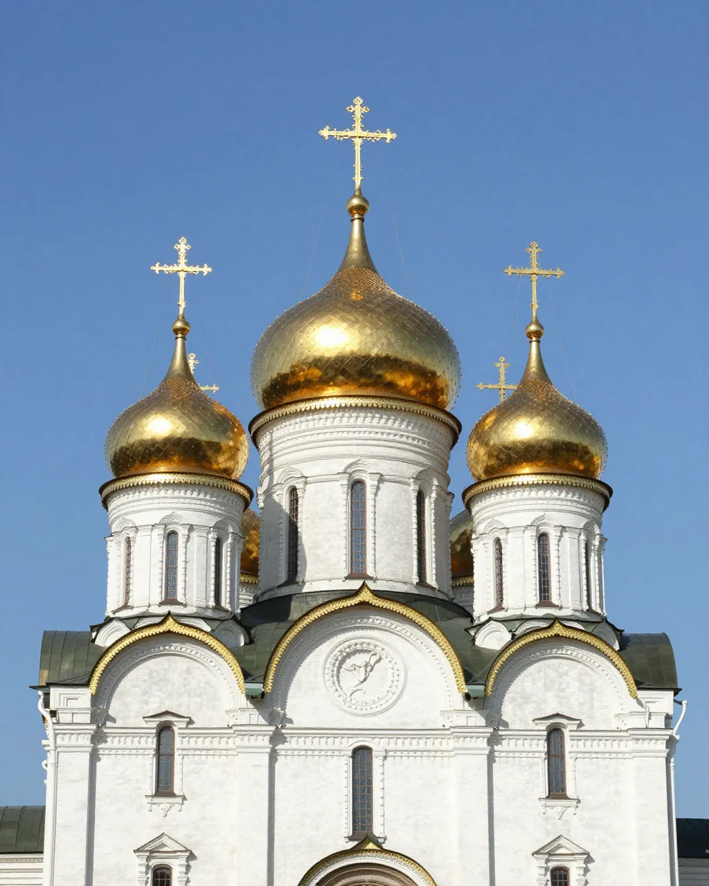 White orthodox church with shiny golden onion domes against a clear bright blue sky