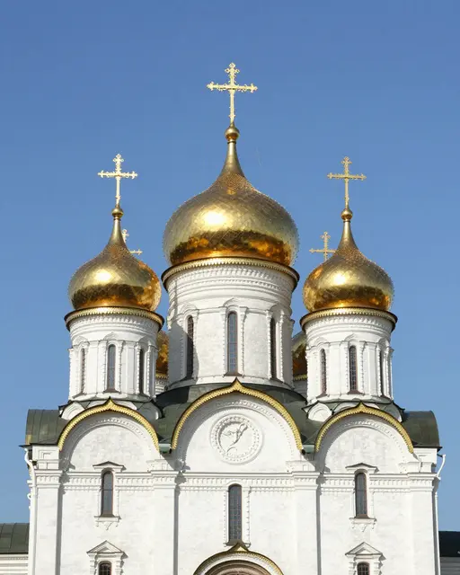 White orthodox church with shiny golden onion domes against a clear bright blue sky