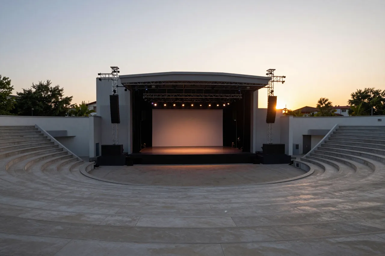 An empty concrete outdoor amphitheater faces a softly lit stage under a gradient sunset sky