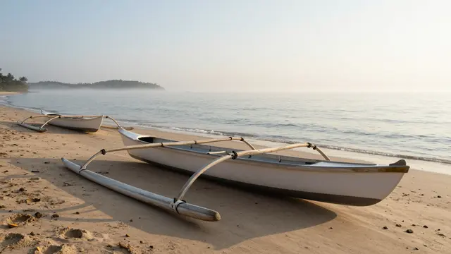 Two small outrigger canoes rest on a sandy beach beside calm misty ocean at sunrise