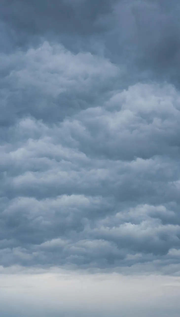 Vertical frame of heavy layered overcast clouds with a pale soft band near the lower horizon