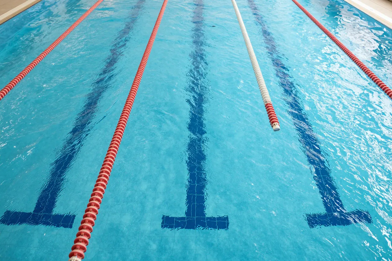 High-angle view of clear turquoise indoor swimming pool marked with lane dividers and tiled lane markers