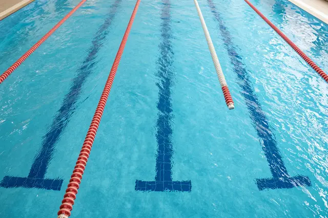 High-angle view of clear turquoise indoor swimming pool marked with lane dividers and tiled lane markers
