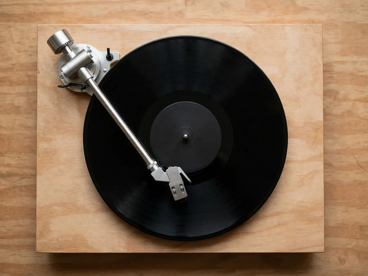 Overhead shot of a wooden base record player with tonearm resting on a plain black vinyl record