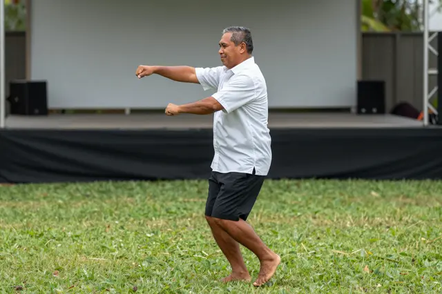Side view of a barefoot Pacific Islander man dancing on grass in front of an outdoor stage
