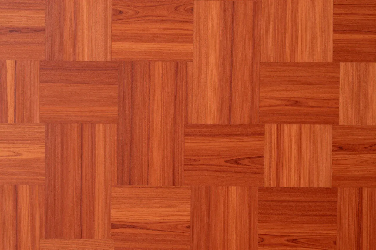 Full frame flat close-up of interlocked orange-red padauk wood parquet with a smooth satin finish
