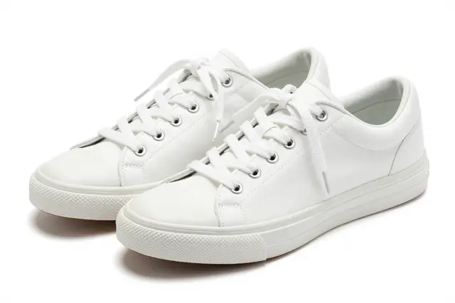 Two plain white canvas sneakers with loosely tied laces sit isolated on a pure white studio background