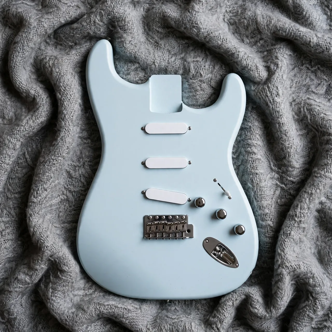 Overhead view of a pale light blue electric guitar body resting on a textured gray wool blanket