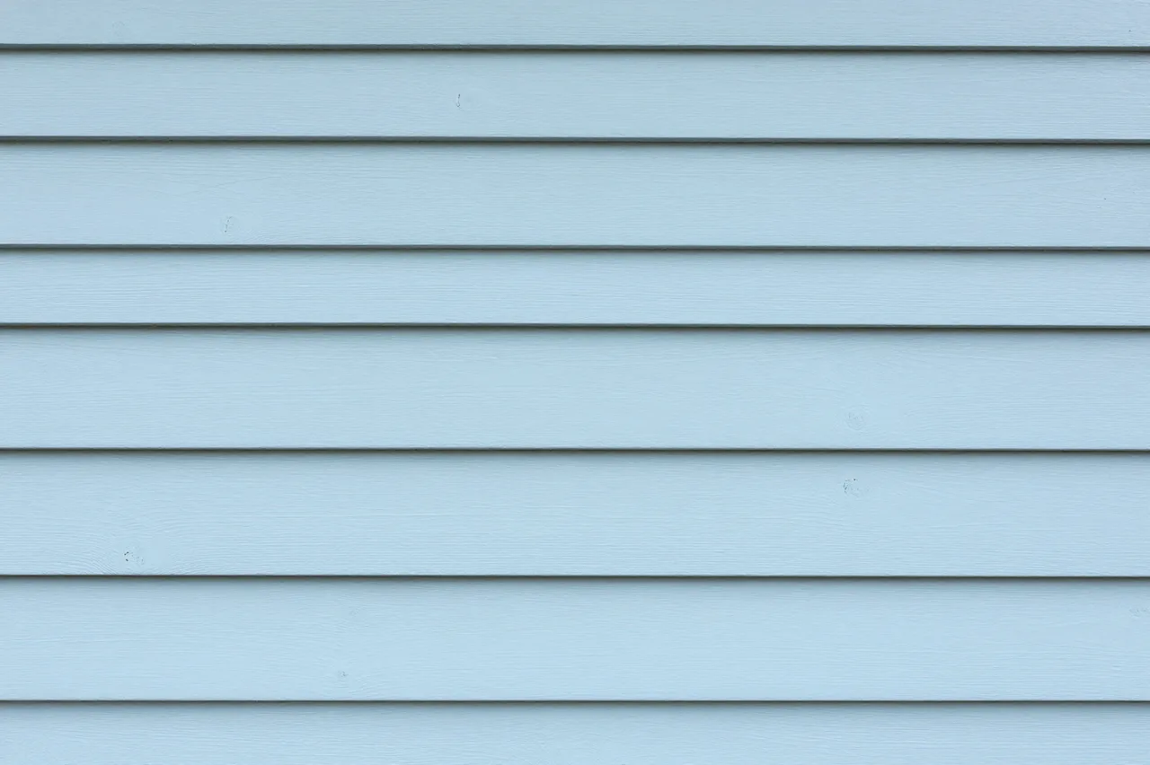 Full frame close-up of horizontal pale light blue wooden siding planks with thin dark gaps between each board