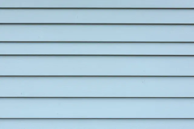 Full frame close-up of horizontal pale light blue wooden siding planks with thin dark gaps between each board