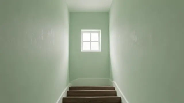 Empty pale green painted stairwell with dark wood steps and soft light from a small upper window