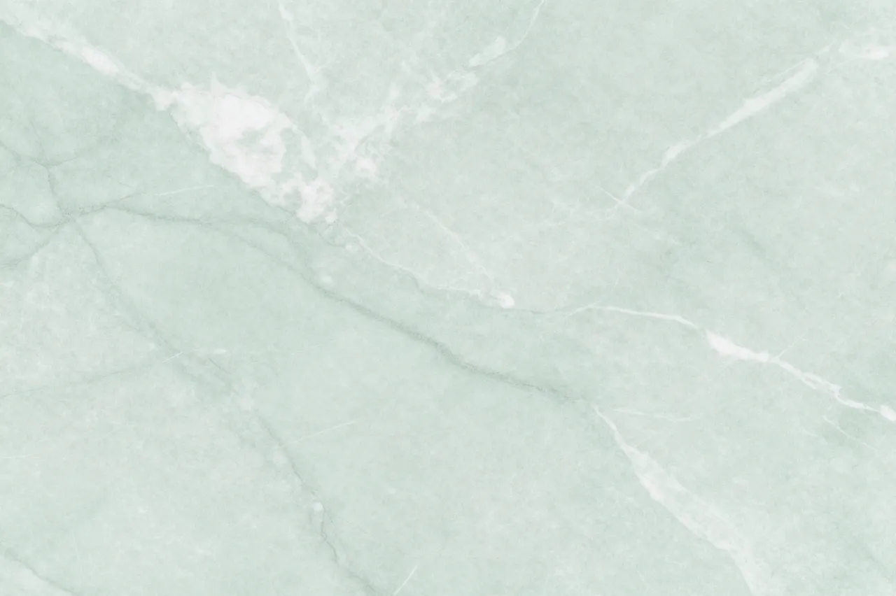 Full frame view of a polished pale mint green marble surface with soft cloudy white veining