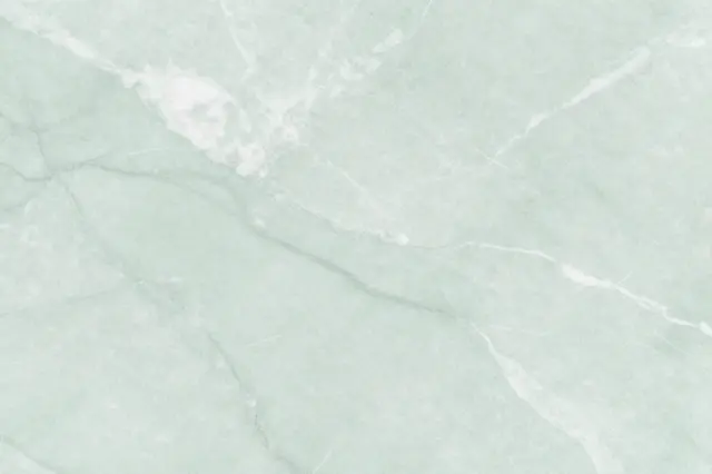 Full frame view of a polished pale mint green marble surface with soft cloudy white veining