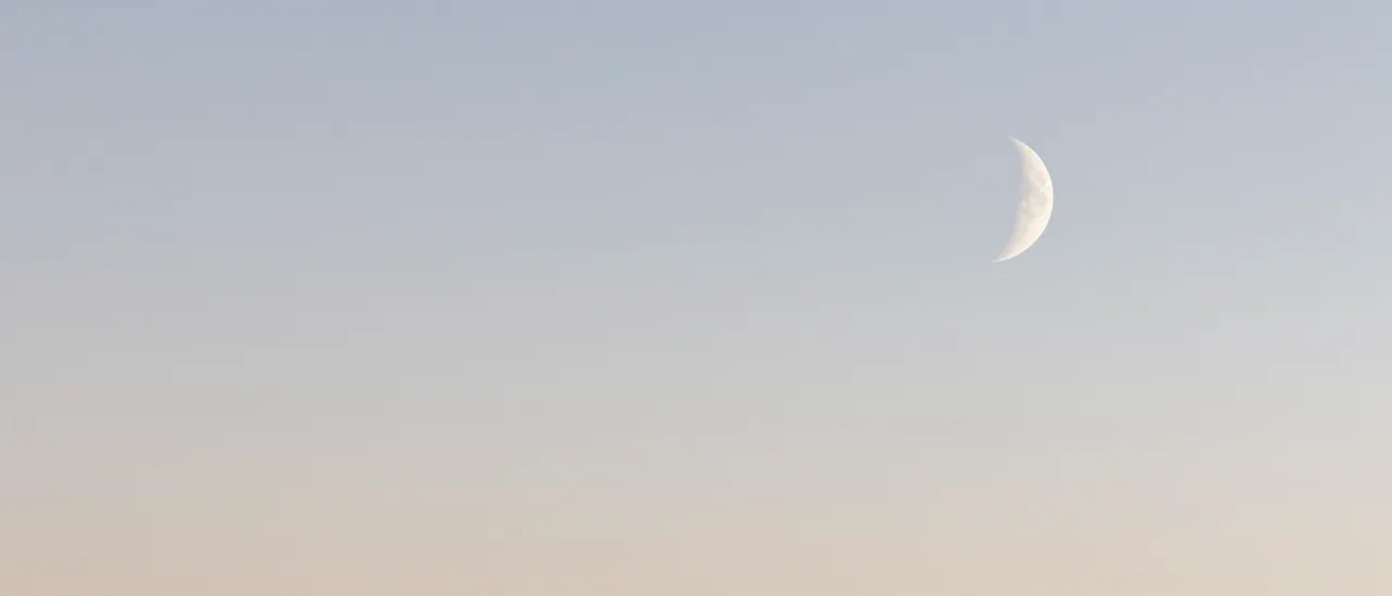 A soft gradient pale pastel sky features a thin crescent moon positioned at the right side with empty copy space on the left.