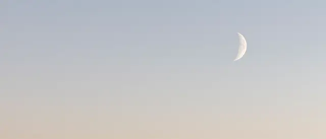 A soft gradient pale pastel sky features a thin crescent moon positioned at the right side with empty copy space on the left.