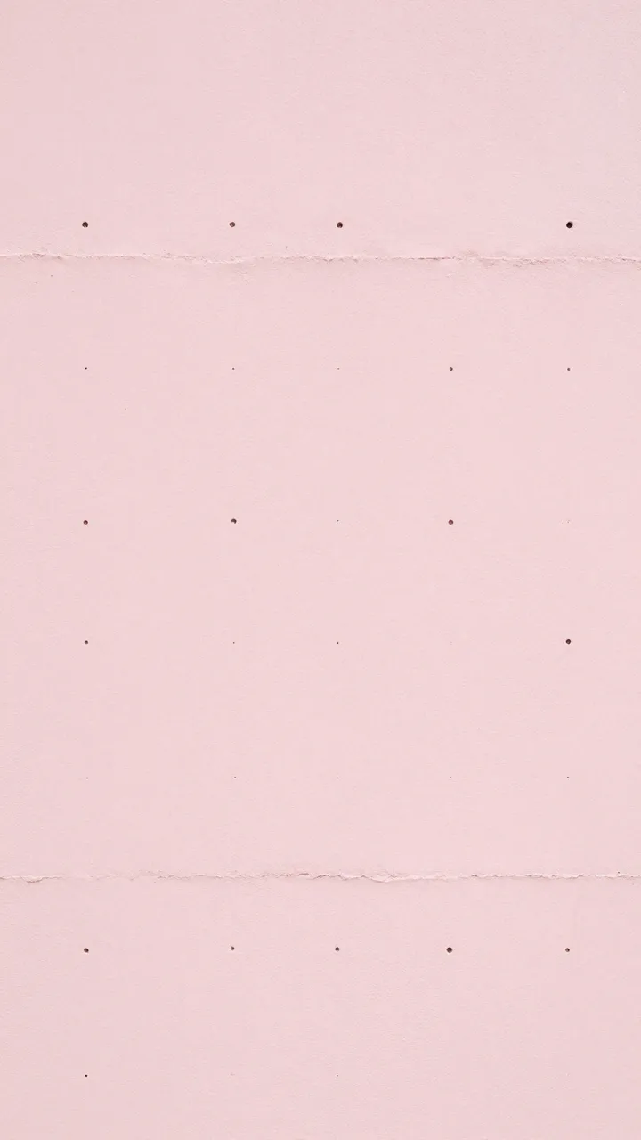 Full frame close-up of pale pink textured paper with evenly spaced small perforations and horizontal torn edges