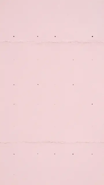 Full frame close-up of pale pink textured paper with evenly spaced small perforations and horizontal torn edges
