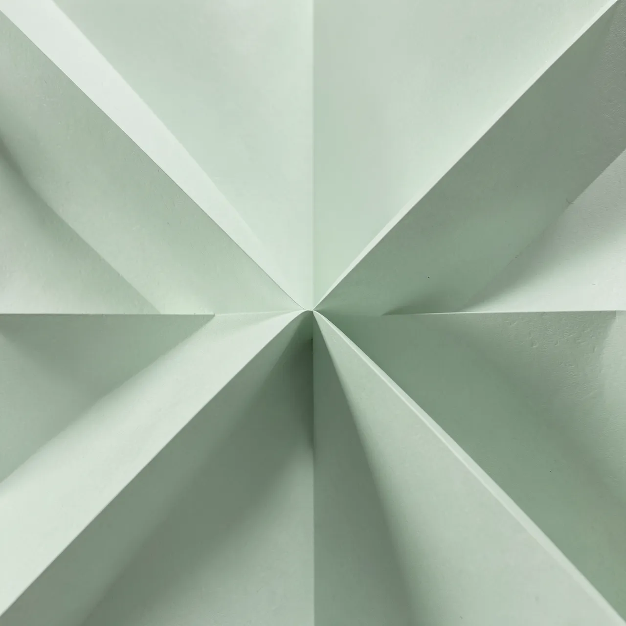Symmetrical folded pale sage paper pleats with soft geometric shadows converging at the center