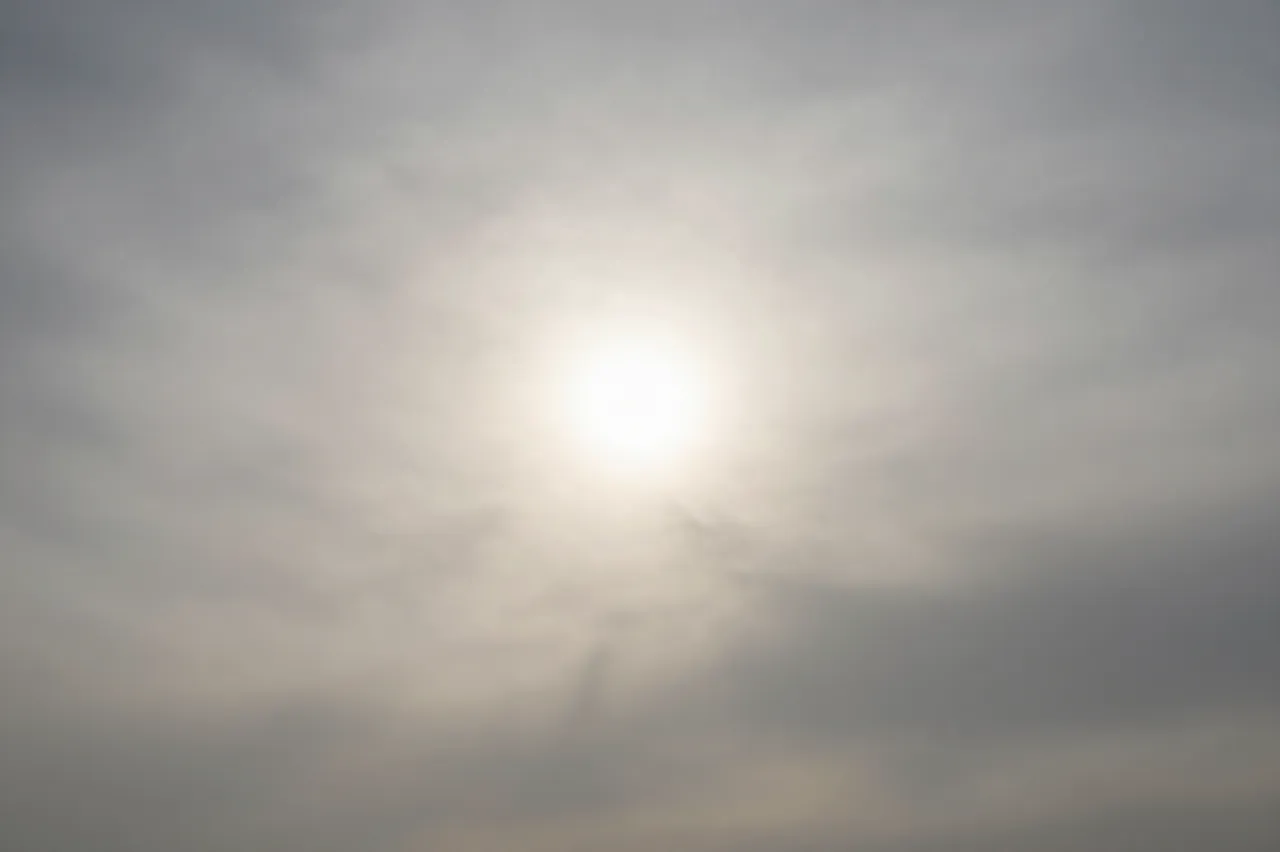Diffuse pale sun shines through a hazy veil of thin high-altitude clouds