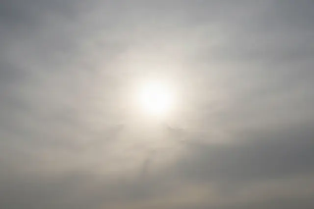 Diffuse pale sun shines through a hazy veil of thin high-altitude clouds
