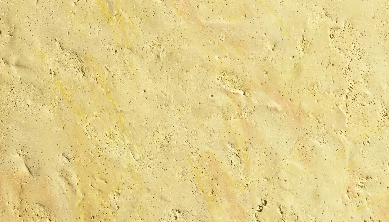 Full frame close-up of a sun-warmed pale yellow matte plaster wall with subtle streaks and fine pits
