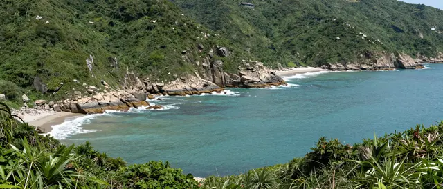 Elevated view of a lush green rocky coastline curving around turquoise ocean coves with small sandy beaches