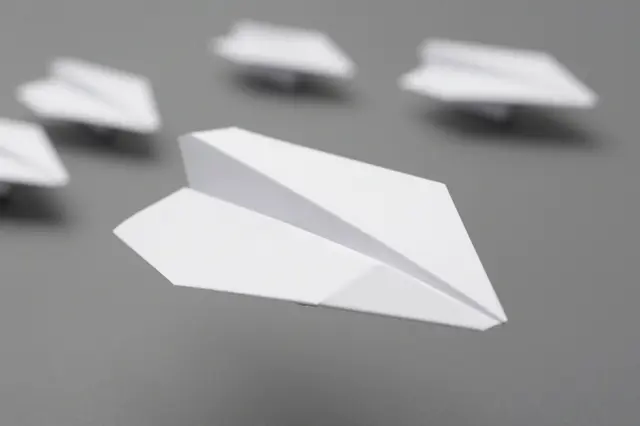 A sharp foreground white paper airplane leads a blurred line of other paper airplanes above a plain gray surface