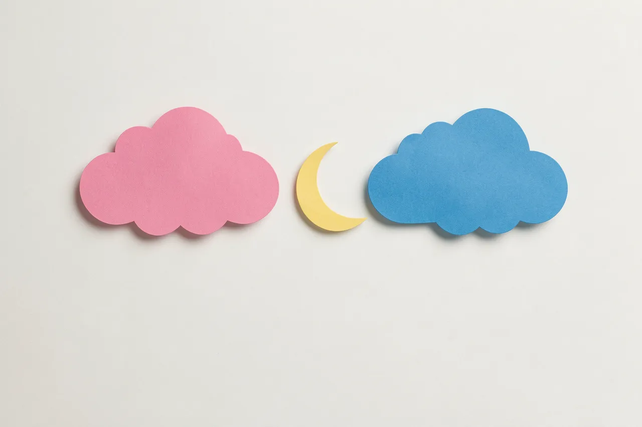 Flat lay of paper cut pink cloud, yellow crescent moon, and blue cloud on an off-white background with empty space below.