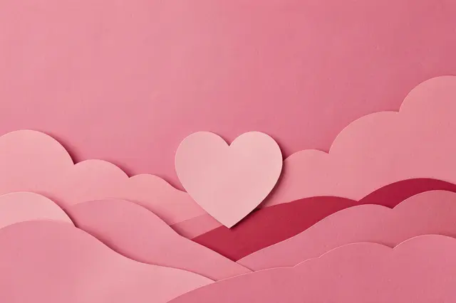 Layered paper craft scene with a pink heart and copy space over soft paper hills and a pink sky background