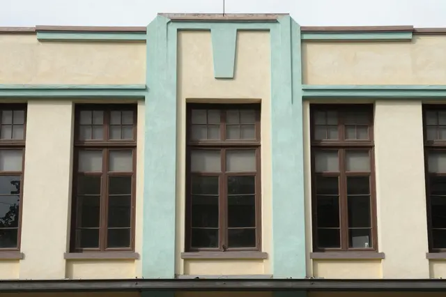 Close-up of a pastel yellow and turquoise art deco building facade with brown framed windows