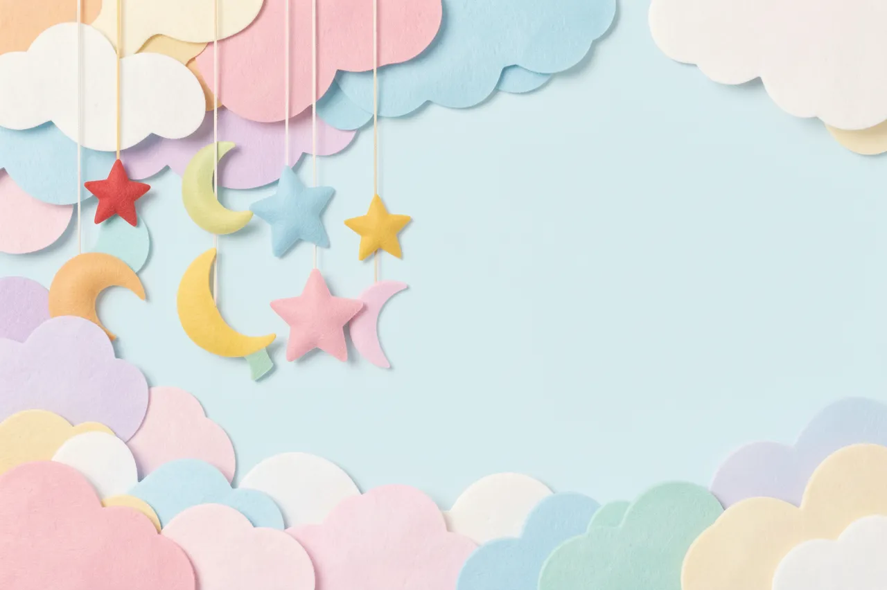 Felt star and moon baby mobile hangs over layered pastel clouds with blank copy space on a light blue background.