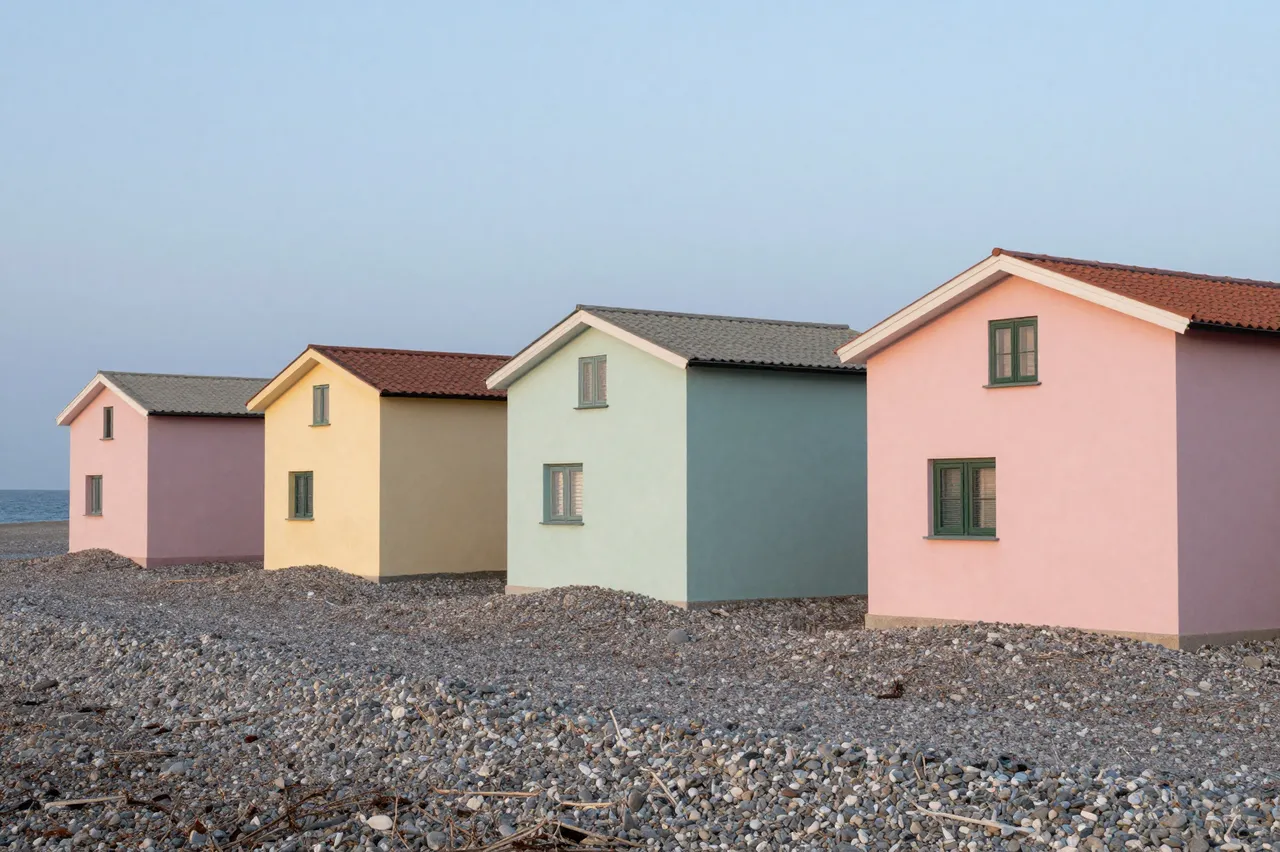 Row of pastel colored small houses perched on a pebble beach beside the calm sea at pale dusk