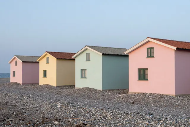 Row of pastel colored small houses perched on a pebble beach beside the calm sea at pale dusk