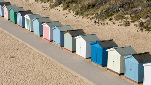 Aerial view of a paved beach promenade lined with neat rows of pastel colored beach huts on sand