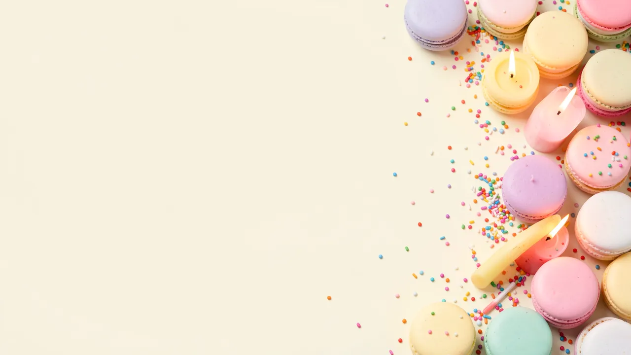 Empty pale vanilla copy space sits left, with pastel macarons, lit candles and sprinkles lining the right edge of the frame.
