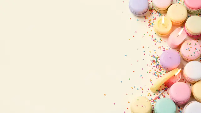 Empty pale vanilla copy space sits left, with pastel macarons, lit candles and sprinkles lining the right edge of the frame.