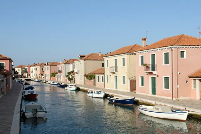 A quiet canal lined with pastel waterfront houses and moored small boats under a clear bright afternoon sky