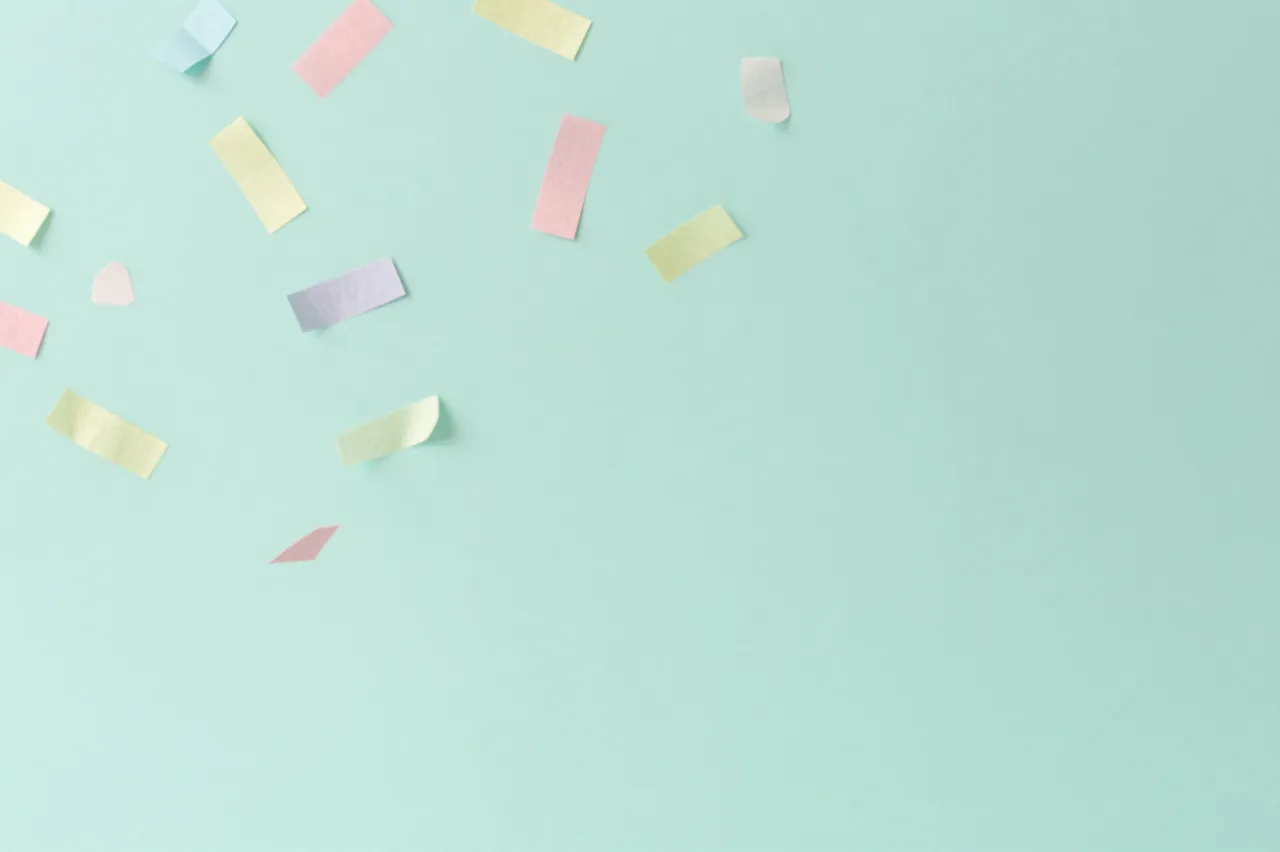 Delicate pastel paper confetti drifts across a smooth solid mint green background with empty copy space
