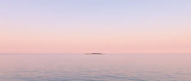 Wide view of a calm flat sea with a tiny distant island under a soft pastel gradient dawn sky