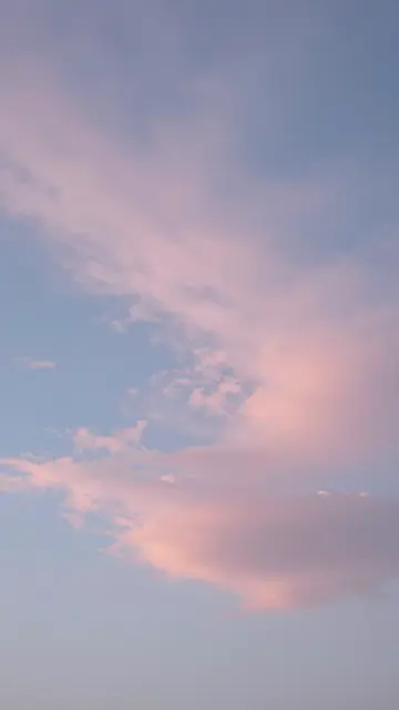 Soft pastel pink and wispy blue clouds fill the sky viewed straight up at early dawn